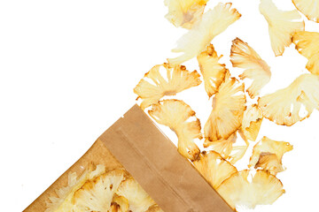 pieces of dried pineapple on a transparent white background spilled out of paper eco-friendly packaging. Healthy food and snacks. Organic fruit