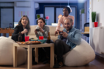 Multi ethnic group of coworkers play game on console while holding joystick. Cheerful diverse...