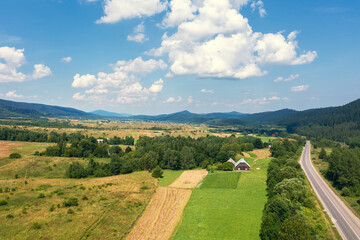 Obraz premium Aerial view of a mountain valley. Rural landscape in summer. View of the village, highway, and mountains on a sunny day
