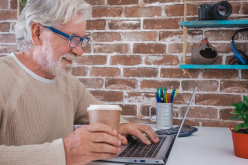 Portrait of smiling senior man using laptop computer at home . Brick wall on background