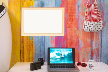 Obraz premium Desktop with laptop computer and photograph of a young surfer. Concept of summer and beach holidays