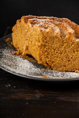 Top view of half yogurt sponge cake on dark plate, on wooden table and black background, in vertical, with copy space