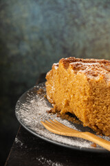 Top view of half yogurt sponge cake on dark plate with sugar and wooden fork, on wooden table and gray background, in vertical, with copy space