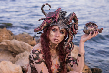 beautiful girl in the costume of the sea witch Ursula, holding a fish in her hand, against the background of the sea, close-up, portrait