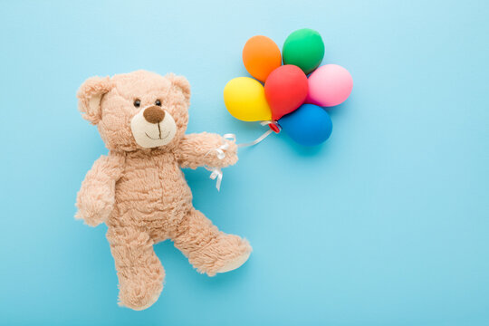 Naklejka Smiling brown teddy bear holding heap of colorful balloons on light blue table background. Pastel color. Closeup. Congratulation concept. Top down view.