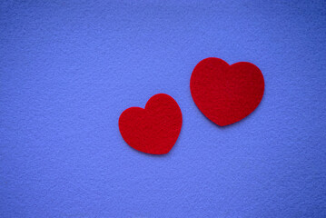 Two red textile hearts made of felt fabric on a purple background, a place for a congratulatory text