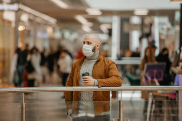 A man in a face mask is holding a cup of coffee in the shopping center.