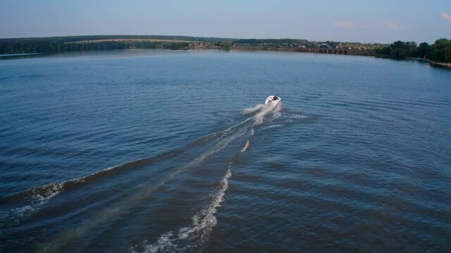 Boat on water surface at sunset. People driving the motor boat quickly along the evening river on beautiful water background. Aerial view