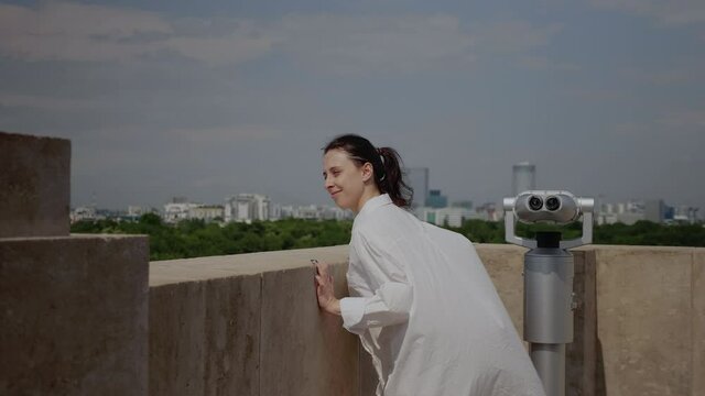 Caucasian woman admiring panoramic view of modern town while standing on top of skyline tower. Young adult looking at urban landscape from observation point on high building roof