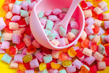 Children's tableware silicone bowl with spoon. Serving baby food, kid dishware.Pink silicone bowl and spoon are in a heap of sweets and marmalade. bright, colorful photo flatly