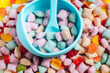 Children's tableware silicone bowl with spoon. Serving baby food, kid dishware.blue silicone bowl and spoon are in a heap of sweets and marmalade. bright, colorful photo flatly