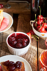 Cherry pie with jam in a bowl. Tea, flowers. Wooden background, side view