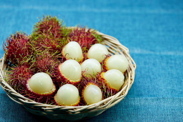 closeup ripe rambutan fruits in wicker basket isolated on blue tablecloth