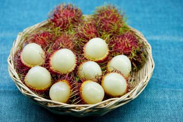 closeup ripe rambutan fruits in wicker basket isolated on blue tablecloth