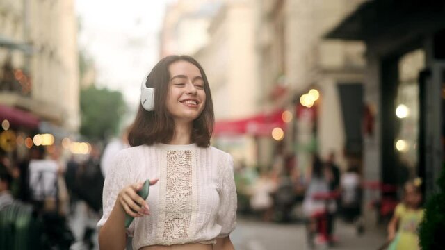 Happy cool woman wearing headphones dancing alone on street. Young adult happy girl sing and funny dancing in downtown very emotional. Modern lifestyle and happiness concept