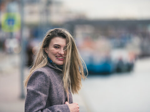Attractive smiling, contented young woman in coat with tousled hair