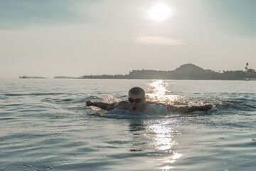 A sports man is engaged in swimming on the sea. Breaststrokes across the ocean at dawn