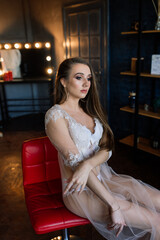 Bride morning preparation. Beautiful young woman in white wedding negligee in a dark studio