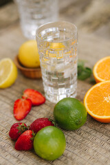 A tall glass cup of water with ice. Sliced oranges, lemons, lime and strawberry. Close up