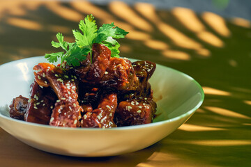 Pork ribs in sweet and sour sauce with cilantro, sesame seeds and Sichuan pepper in a white bowl. Chinese cuisine