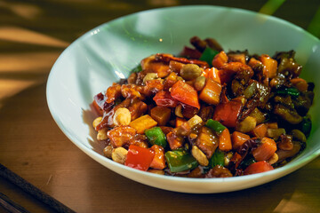 Sweet and sour chicken with wok vegetables, sesame peanuts and Sichuan pepper in a white bowl. Chinese cuisine