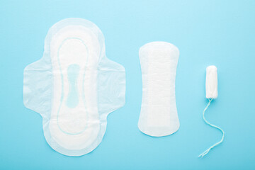 New white sanitary towel, panty liner and tampon on light blue table background. Pastel color. Closeup. Female hygiene products. Top down view.