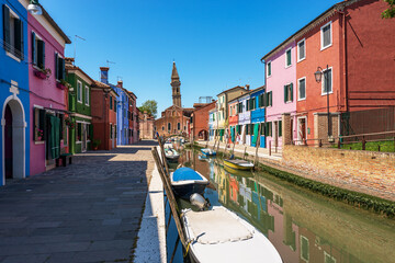 Fototapeta na wymiar Burano island, small canal with moored boats and colorful houses. Church of San Martino with leaning bell tower. Venetian lagoon, Venice, UNESCO world heritage site, Veneto, Italy, Europe.