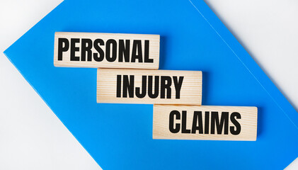 There is a blue notebook on a light gray background. Above are three wooden blocks with the words PERSONAL INJURY CLAIMS.
