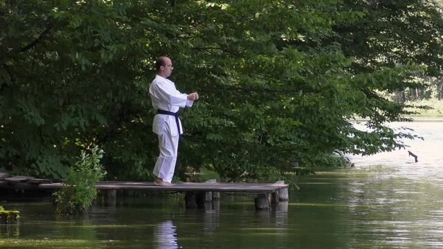 A man athlete trains four kicks on the bridge against the backdrop of a pond