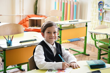 Happy smiling boy is drawing and going to school for the first time. Child with school bag and book. Kid indoors of the class room with blackboard on a background. Back to school.