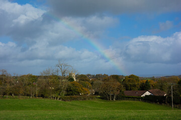 Fototapeta na wymiar rainbow over Devon village and church with blue sky and clouds