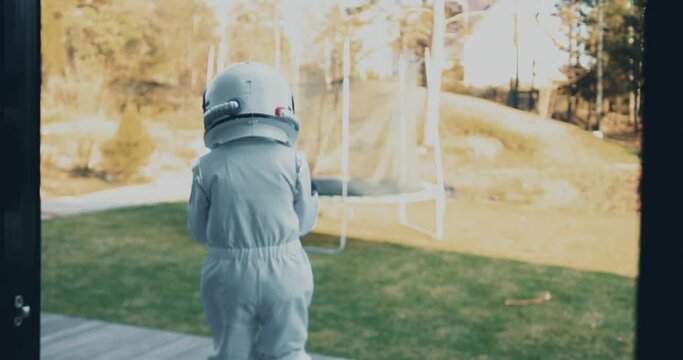 Camera follows little kid run out of house glass door with dog to terrace wearing white astronaut space suit and helmet.