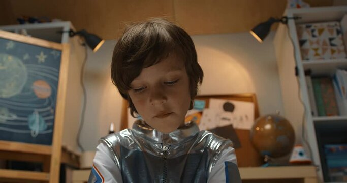 Portrait of happy creative 5-7 little boy in space suit playing with little piece of silver tin foil. Dreaming of future