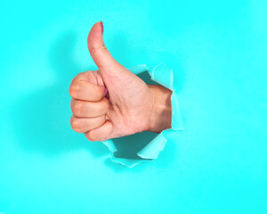 Woman hand finger up in whole of torn blue paper background