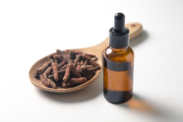 Bottle of Extract and long piper in wooden spoon on white background.