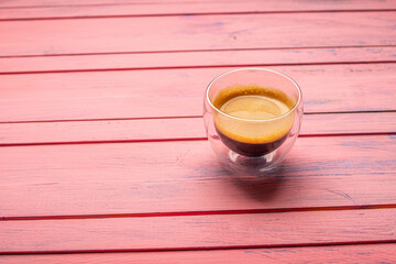 Coffee in glass cup on pink wooden background