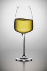 A close-up of crystal glass with white wine on the light background. Wavy surface, no splashes. Restaurant glassware, beverage, table setting, romance, passion, love, party, water splashes.
