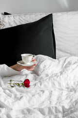 Fototapeta na wymiar Female hand with cup of coffee and red rose in white linen