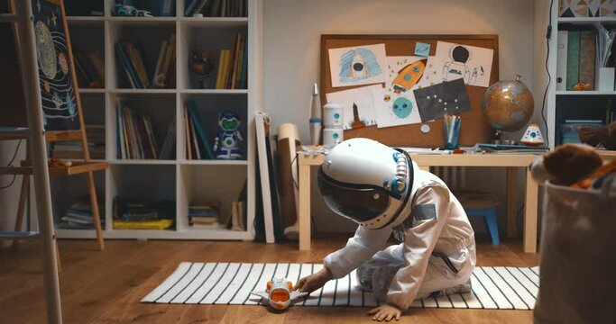 Dreaming of space travel. Happy little child in astronaut suit, helmet playing rocket ship pilot, flying toy in his room