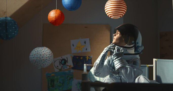 Atmospheric shot, boy child wakes up wearing space suit in bed, looking up at morning sun light and closing helmet visor