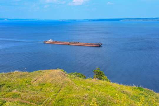 An articulated tugboat and barge bulk carrier transports sand and construction materials on the river. The large barge sails along the wide Volga river. Transportation industry.
