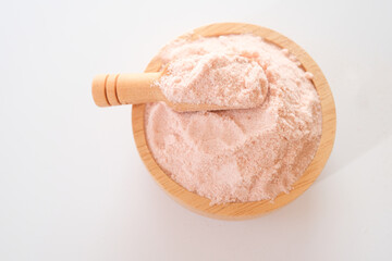 Top view of Himalayan pink salt powder in wooden bowl and scoop isolated on white background. 