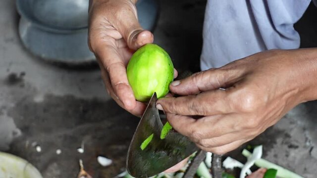 A woman peels a Hog plum fruit using a traditional cutting tool. A unique cutting instrument Boti of the Indian subcontinent. Rural widely used sharp blade vegetable and fish cutting tools. 