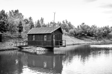 Old wooden house on a lake. Isolated building in nature. Arstistic photo with retro and melancholic vibes. Black and white image.