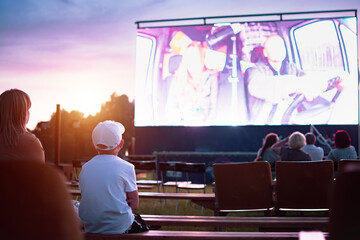 A boy in a cap watching a movie in the open air
