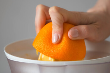 Woman is squeezing oranges using electric juicer in the kitchen, hand closeup. Healthy vegan ripe fruit juice, natural vitamins from food. Making orange juice pressing half of orange.