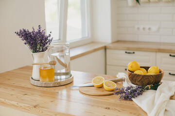 Fresh lemons, jar with honey and bunch of lavender flowers in a vase standing on a kitchen table at home. Ingridients for making lemonade.