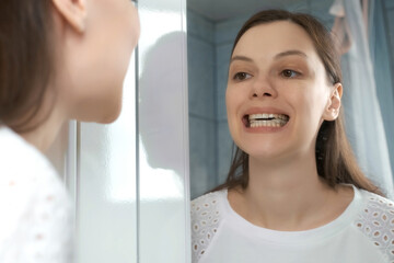 Young woman is installing splint for down teeth to correct the bite looking at mirror in bathroom....