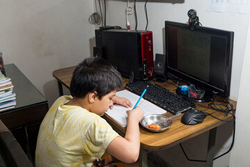 An eight year old Indian boy at home  due to lock down because of corona virus studying in an online class on a desktop computer with a webcam   and having his breakfast along with the session