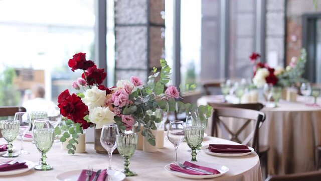 Decoration of the wedding table with red and pink flowers on a white tablecloth. Green glass goblets and framed table number.